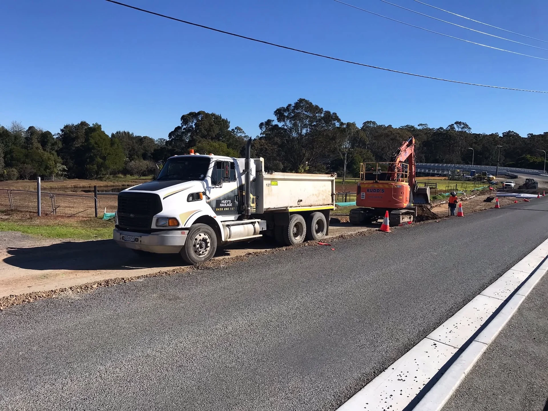 Huey's Haulage tipper truck parked beside an excavator on a roadworks site
