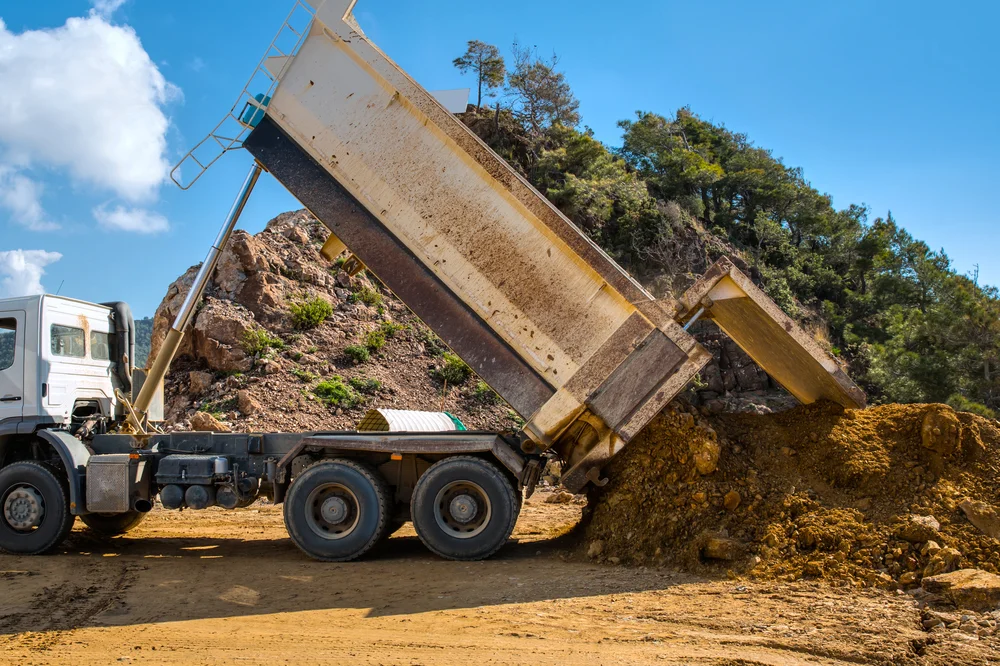 Tipper truck emptying a load of dirt onto a hillside worksite
