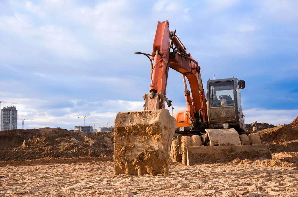 Orange tracked excavator resting its bucket on cleared earth at a large construction site